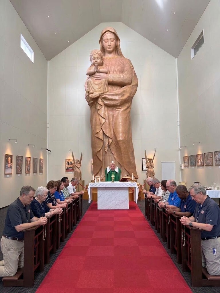 Pilgrims praying during Mass before a large carved wooden statue of Mary and the Child Jesus at Hara Castle Holy Maria Kannon Hall