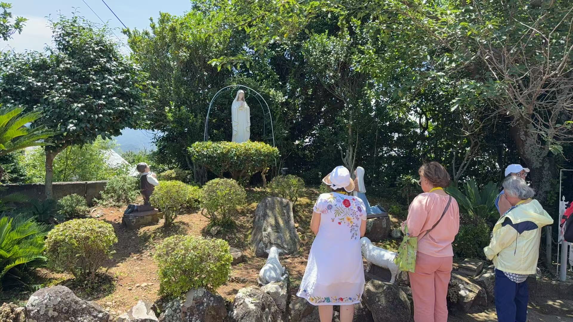 Pilgrims praying before a statue of Our Lady in a peaceful garden in Japan