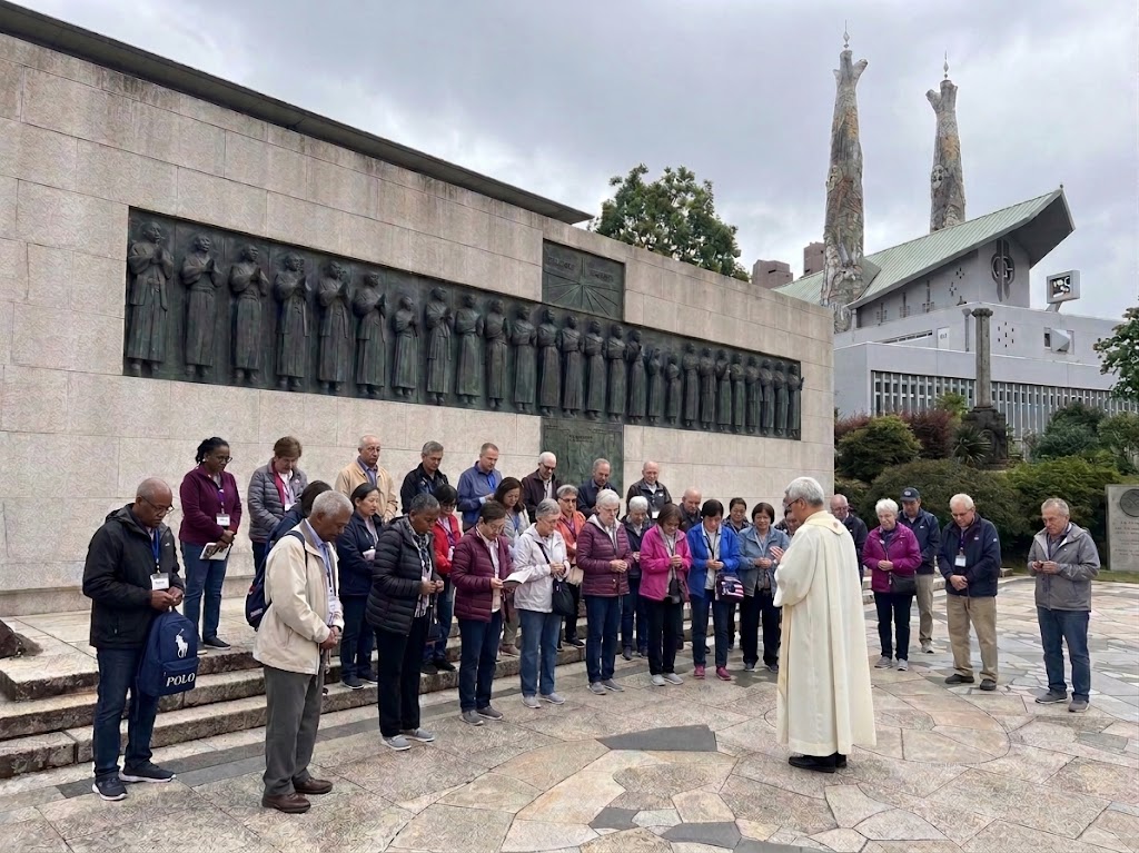 Pilgrims praying with a priest at the Twenty-Six Martyrs Monument in Nagasaki